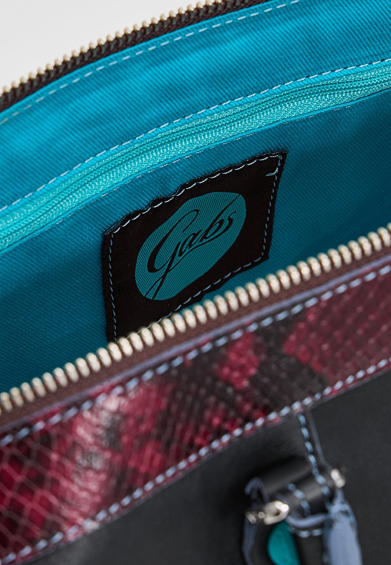Interno di borsa in pelle nera con una vivace fodera turchese, cerniera dettagliata e un accento testurizzato color borgogna con etichetta logo Gabs.