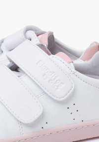 Sneaker in pelle bianca con dettagli rosa. Include due ampie cinghie in velcro, perforazioni per la traspirabilità e una suola di gomma testurizzata.