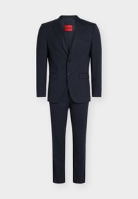 Σκούρο ναυτικό μπλε ανδρικό κοστούμι με δύο κουμπιά, γιακά με εγκοπή, τσέπες με καπάκι και κόκκινη ετικέτα HUGO μέσα στον γιακά του σακακιού.