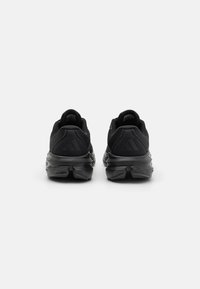 Chaussures de sport noires avec un dessus texturé, un talon arrondi et un logo proéminent à l'arrière. La semelle est dotée d'un amorti segmenté pour le soutien.