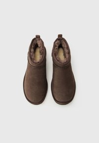 Pair of brown suede ankle boots with soft, plush beige interior lining, flat soles, and pull tabs at the back, shown from above on white background.
