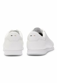 Valkoiset urheilukengät, joissa on sileä nahkapinta, pyöreä kanta, hienovaraiset ompelut yksityiskohdat ja teksturoitu kumipohja.