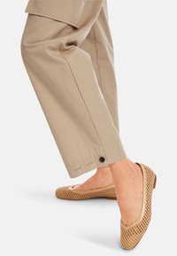 Ballettschuhe in hellem Beige, mit einem geflochtenen Muster und glatten Lederakzenten, kombiniert mit entspannten beigefarbenen Hosen und einem knöpfen-verzierten Saum.
