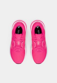 Chaussures de sport rose vif avec une tige en mesh texturée, un col matelassé et des semelles blanches. Elles présentent un design à lacets et une semelle intérieure rembourrée.