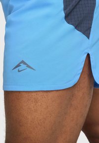 Helle blaue Sportshorts aus weichem Stoff, mit einem dunkelgrauen Netzpaneel, seitlichem Schlitz und einem grauen Nike-Logo am Saum.