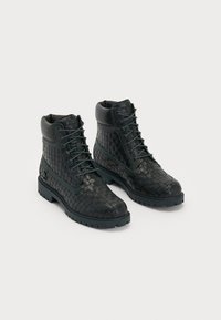 Black woven leather ankle boots with a round toe, lace-up design, and rubber sole; features a smooth leather collar and patterned texture.