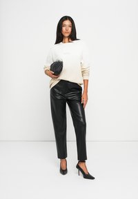 Sweter w odcieniach ombre kremu i beżu, czarne spodnie z sztucznej skóry, czarna torebka o wyraźnej strukturze oraz szpilki w szpic. Prosty design i neutralne kolory.