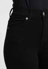Jeans negros de talle alto con una textura suave, embellishments en plata, diseño de cinco bolsillos y presillas para cinturón en la cinturilla.