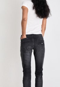 Jeans de mezclilla negros de corte ajustado, con bolsillos traseros y costuras sutiles. Combinados con una blusa blanca de mangas cortas ceñida y con relieve.