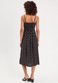 Robe midi noire avec des pois blancs, corsage smocké, bretelles spaghetti ajustables, tissu fluide et ourlet droit.