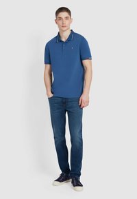 Blauwe polo met contrasterende kraag, korte mouwen en geborduurd logo. Gepaard met donkerblauwe jeans en marineblauwe sneakers.