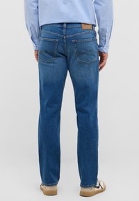 Jeans dżinsowe w średnim niebieskim kolorze o prostym kroju. Posiadają dwie tylne kieszenie z krzywym przeszyciem oraz skórzaną naszywkę przy pasie.