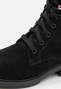 Stivale alla caviglia in suede nero con lacci rotondi, occhielli in metallo e superficie testurizzata. La suola è nera con un leggero tacco per una maggiore stabilità.