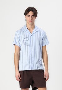 Camicetta a maniche corte con bottoni, caratterizzata da righe verticali blu e bianche, con un design ricamato di un polpo sul lato sinistro. Tessuto leggero.