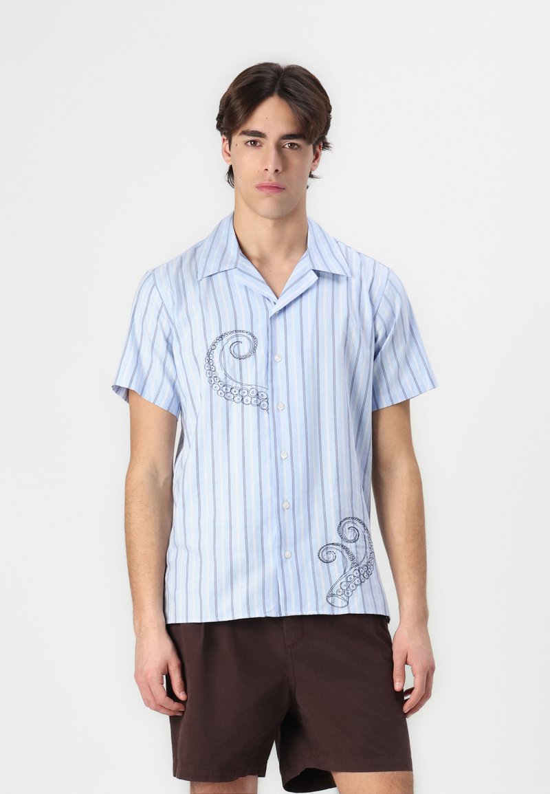 Camicetta a maniche corte con bottoni, caratterizzata da righe verticali blu e bianche, con un design ricamato di un polpo sul lato sinistro. Tessuto leggero.