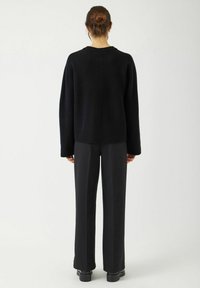 Svart stickad tröja med sjunkna axlar, ribbad nederkant och avslappnad passform, kombinerad med högmidjade svarta byxor och kraftiga svarta skor.