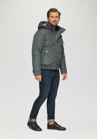 Kurtka puchowa w ciemnoszarym kolorze z kapturem, z kieszeniami na zamek błyskawiczny i kontrastującymi białymi zamkami. W połączeniu z ciemnymi dżinsami i czarnymi trampkami.