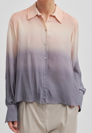 Overhemd met lange mouwen en knopen, met een verloop van perzik naar grijs, los gedragen over beige broek, handen gedeeltelijk zichtbaar.