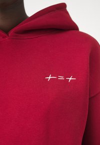 Roter Kapuzenpullover aus weichem Material mit einem weißen gestickten Design auf der Brust. Schlichtes und minimalistisches Design.
