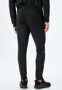 Sorte tapered sportbukser med elastisk talje, glat tekstur og minimal sømdetaljering, parret med sorte træningssko.