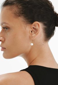Pendiente de aro dorado que presenta una sola perla blanca. Diseño minimalista con metal delgado y elegante, acentuado con una perla lustrosa.