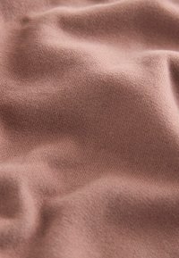 Tissu doux et texturé dans une couleur rose douce, affichant un tricot fin avec des variations subtiles de ton et une apparence lisse.