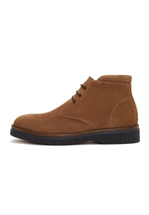 Bottine en daim marron avec semelle en caoutchouc noir et trois œillets pour lacets, vue de profil sur fond blanc.