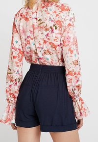 Blouse florale rose et crème avec manches longues à volants, associée à un short bleu marine à taille élastique avec revers roulés et poches arrière.