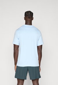 Heled sinise lühikese varrukaga T-särk, mis on valmistatud pehmest kangast ja millel on ümar kaelus. Kandmine tumeroheliste sportlike lühikesed pükstega.