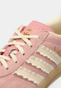 Roze suède sneakers met crèmekleurige gerafelde strepen, witte veters en een gouden logo op de tong. Opvallende textured rubberen zool.