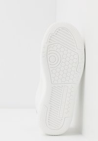 Zapatilla blanca con una suela de goma texturizada, que presenta patrones hexagonales, estrías y marca en la entresuela. Diseño minimalista.