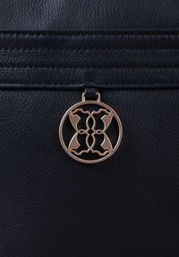 Black leather bag featuring a circular gold-tone metal accent with intricate cut-out design. Textured surface and stitched detailing visible.