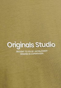 Oliven grøn T-shirt med en glat tekstur, med hvid trykt tekst: "Originals Studio", "Brought to you by JACK&JONES", og "Designed in Copenhagen."