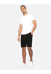 Shorts noirs avec des cordons orange, arborant un petit logo brodé. Associé à un t-shirt blanc uni et des baskets blanches.