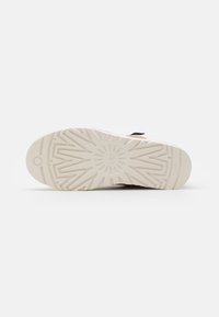 Suela de zapato con un material de goma blanca texturizada. Presenta un patrón de tracción geométrico y un logotipo circular en el centro.
