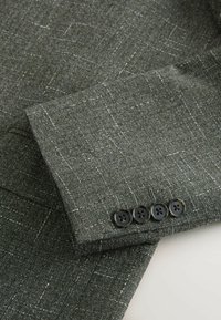 Manche de costume à carreaux gris foncé avec quatre boutons noirs alignés près du poignet.