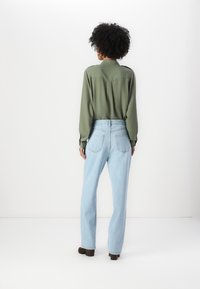 Langermet, olivenfarget skjorte med bakgods og knappedetaljer, kombinert med lyseblå, høy midje jeans og brune hæler støvletter.