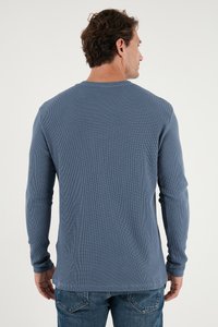 Garā piedurkņu ribu krekls maigi zilā krāsā, ar apaļu kakla izgriezumu un brīvu piegriezumu, kombinēts ar džinsa biksēm.