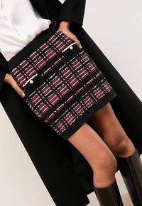 Fekete alapon piros, fehér és szürke kockás mintájú kötött szoknya. Díszítő zsebekkel, kör alakú díszítésekkel és bordázott derékrésszel.