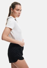 Camisa polo blanca con cuello negro combinada con shorts negros. El conjunto es ajustado, con una textura suave y detalles de diseño mínimos.