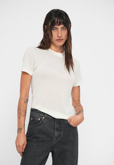 Tricou alb cu mânecă scurtă, cu guler rotund, realizat dintr-un material ușor. Asociat cu blugi gri închis, care au accente din metal.