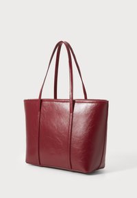 Sac fourre-tout en cuir rouge avec une texture lisse, de forme rectangulaire et des poignées doubles pour le transport. Présente des coutures minimales et aucun matériel.