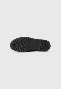 Semelle de botte en caoutchouc noir avec un motif de traction profond, comportant des indentations hexagonales et rectangulaires pour une meilleure adhérence et durabilité.