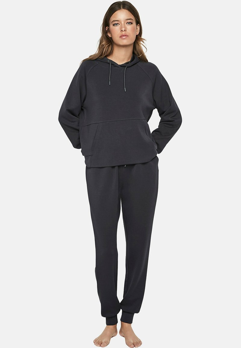 Donkergrijze sweatshirt en bijpassende broekset, gemaakt van zachte stof. De sweatshirt heeft een capuchon en een voorzak; de broek heeft elastische boorden.