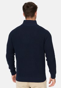 Suéter de punto waffle en azul marino, con cuello alto y puños acanalados. El diseño presenta una superficie texturizada y un corte holgado.