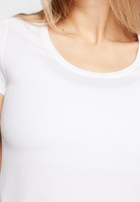 Vitt kortärmat topp i texturerat tyg; har rund halsringning; figurnära design som framhäver överkroppen.