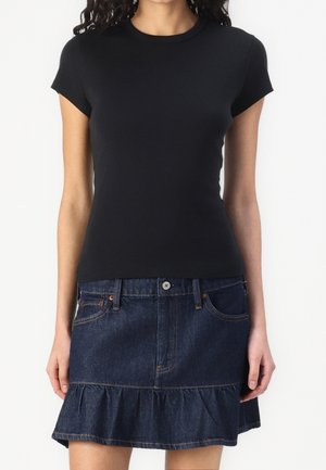 Kobieta ubrana w dopasowaną czarną bluzkę z krótkim rękawem, połączoną z ciemnoniebieską spódnicą dżinsową z falbaną na dole.