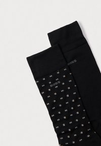 Fekete zokni, egyik oldala egyszínű, a másik oldalán apró fehér és arany négyzetek mintázata látható. Texturált kötött anyag.