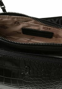 Schwarze, krokodilpräge Ledertasche mit offenem Reißverschluss, der das beige Innenfutter mit aufgedruckten Logos und einem schwarzen rechteckigen Etikett innen zeigt.