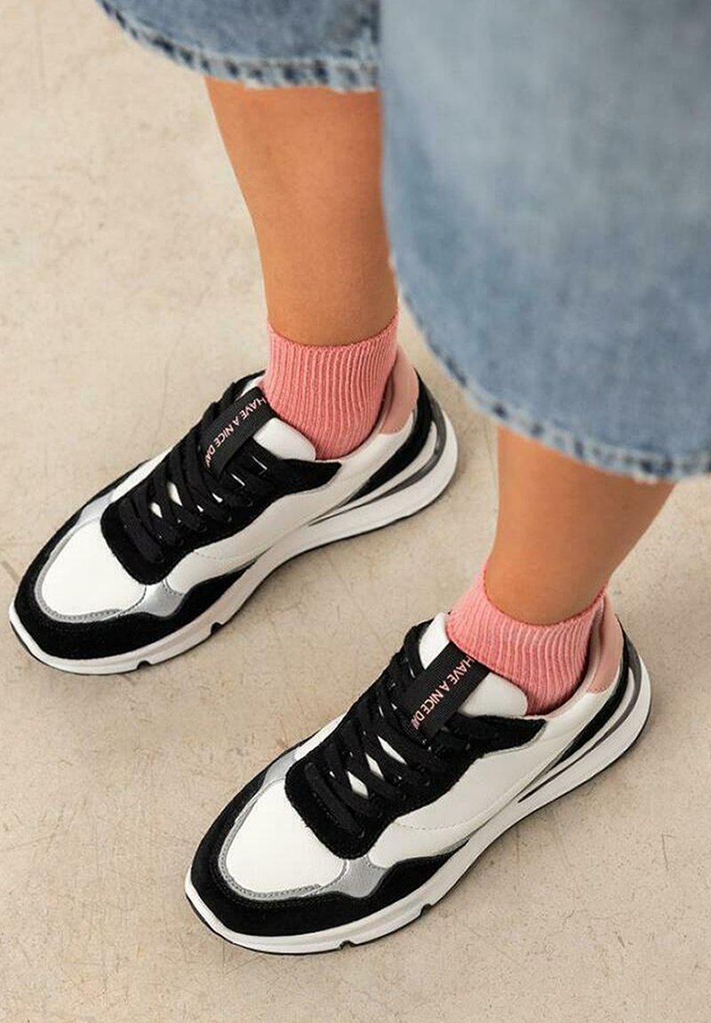 Zapatillas en blanco y negro con materiales de gamuza y cuero, que presentan una suela gruesa, cordones negros y acentos en rosa. Combinadas con calcetines de punto rosa.